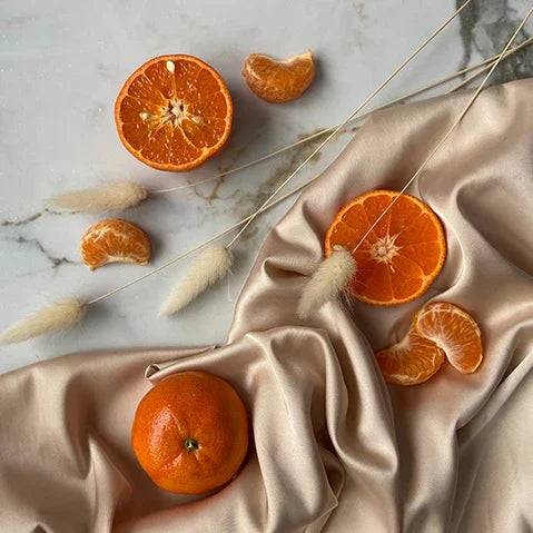 Fresh tangerines and segments on marble with silk fabric and dried grass decor