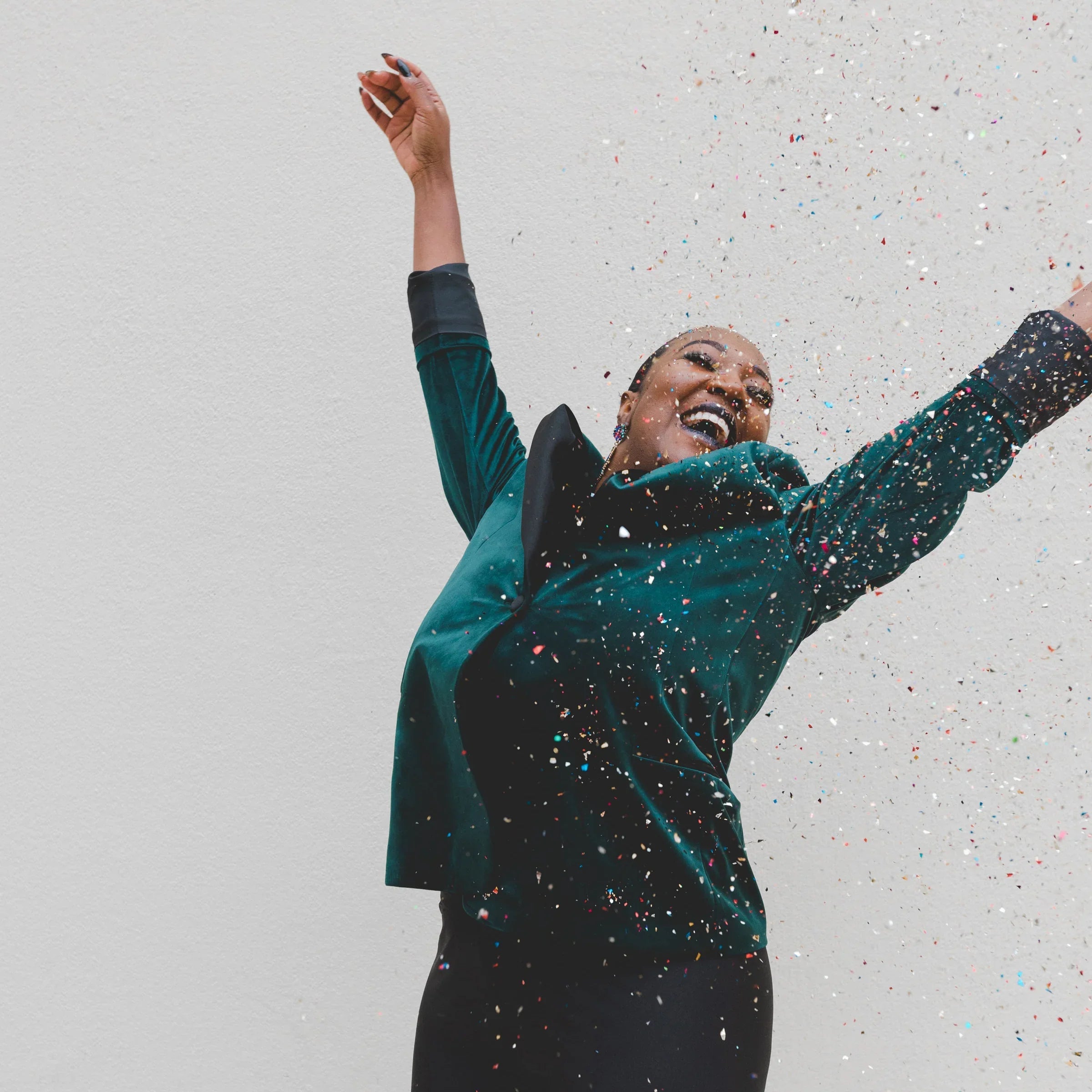 Joyful woman in green jacket celebrating with confetti against a plain white background