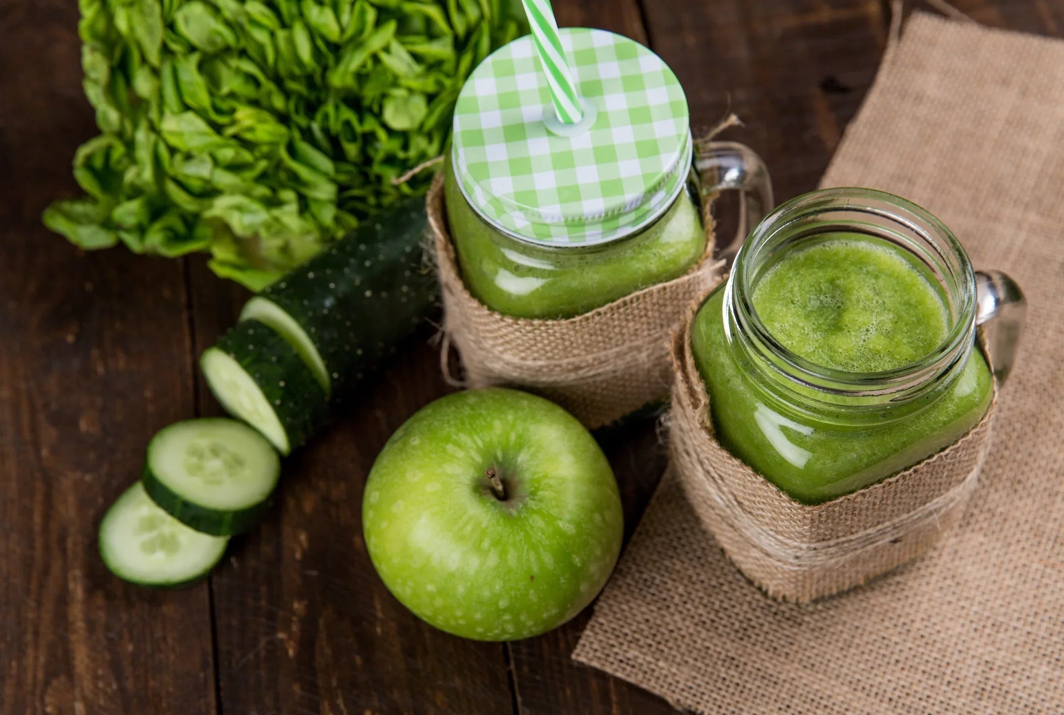 Green juice with apple, cucumber, and lettuce in glass jars on a rustic wooden table