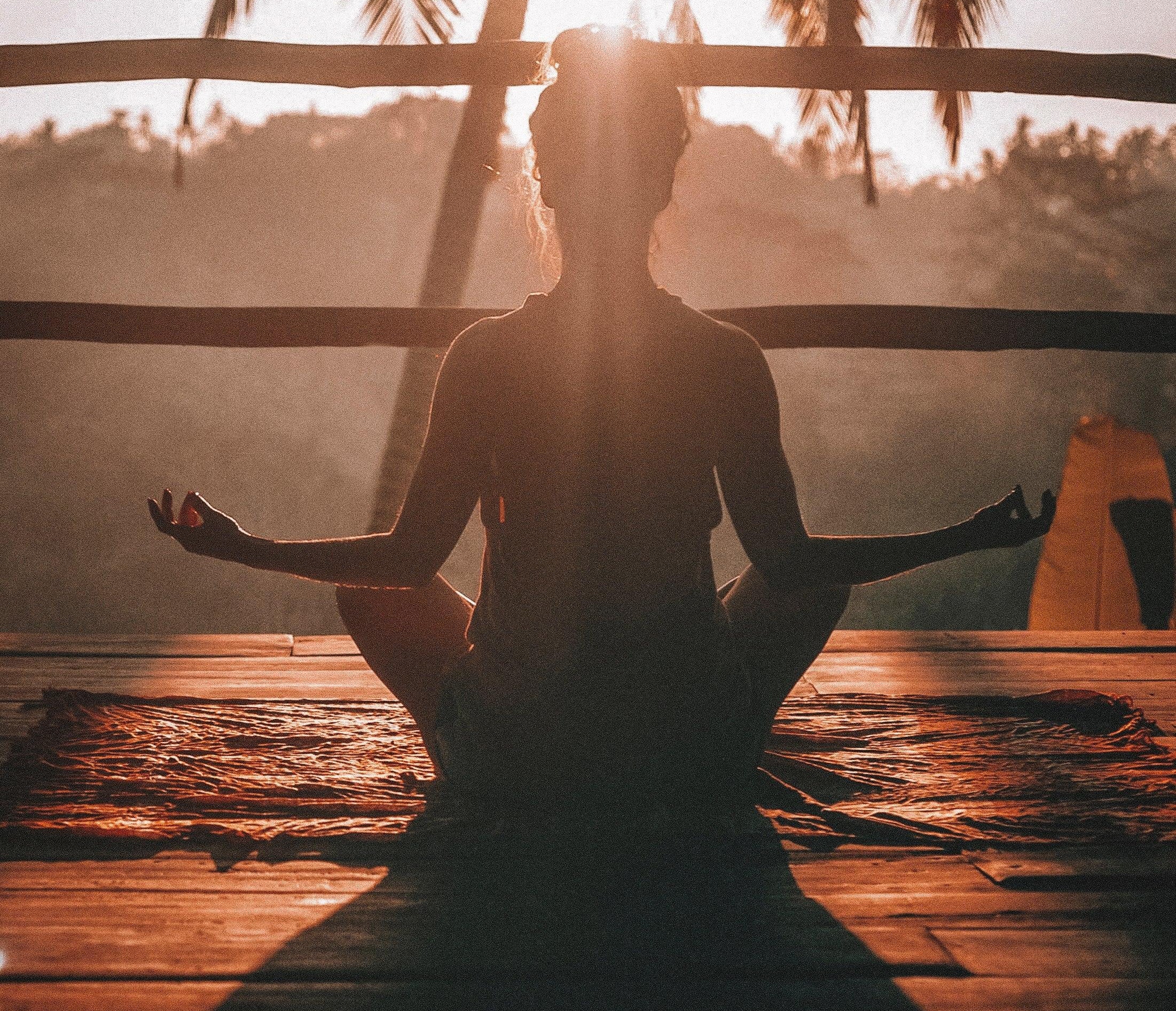Woman meditating at sunrise on wooden deck with palm trees in tropical setting