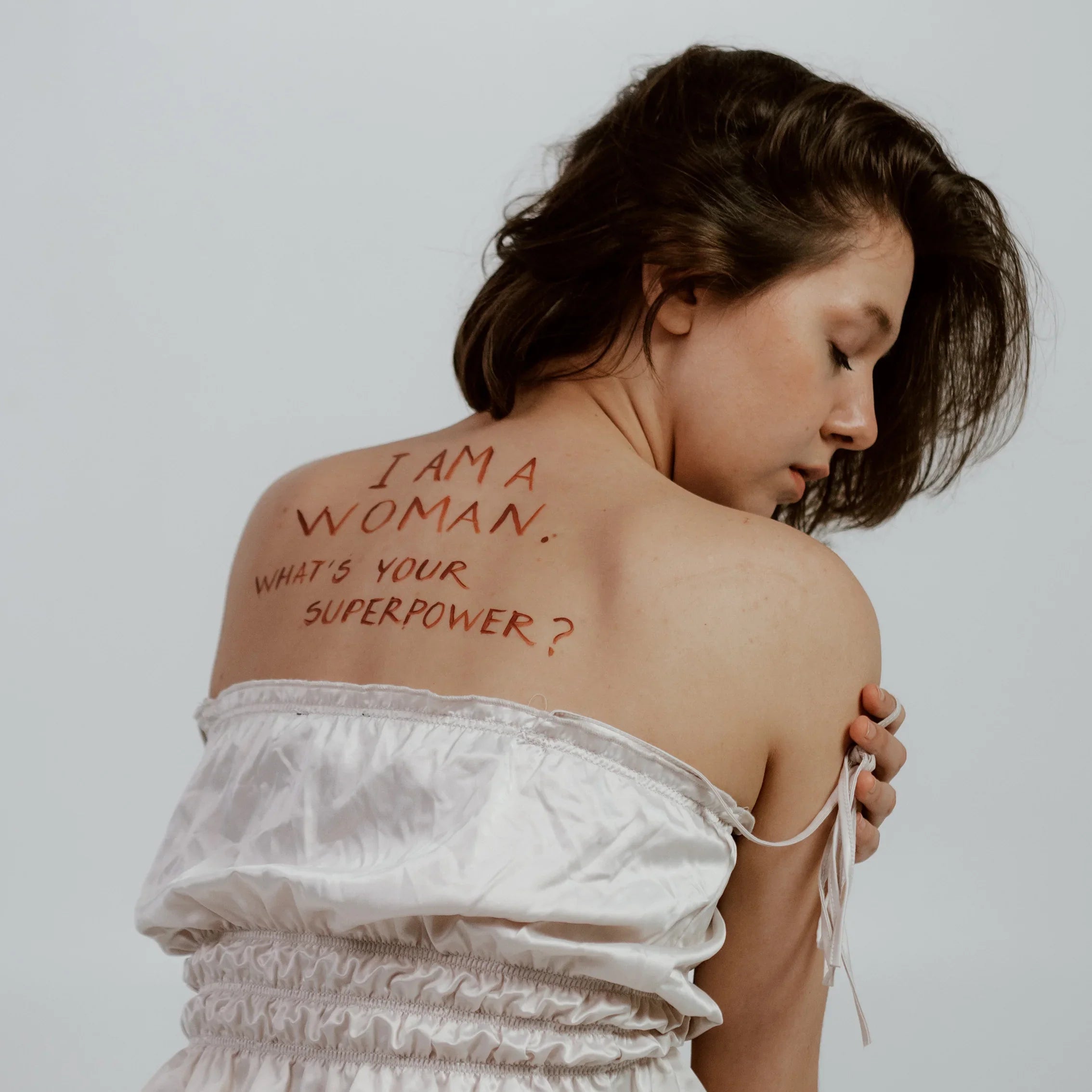 Woman in white dress showing back with empowering message written on skin, minimalist background