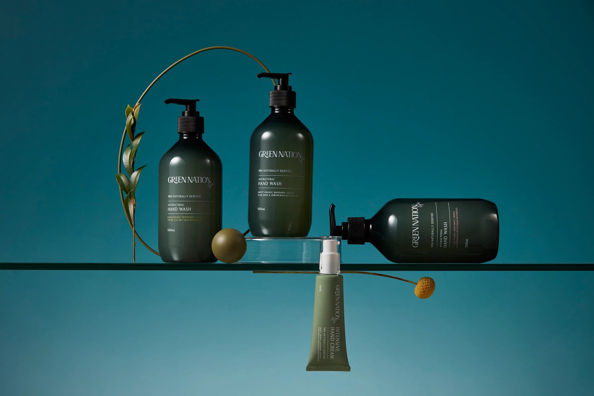 Green Nation Life hand wash and hand care products on glass shelf with botanical decor, teal background