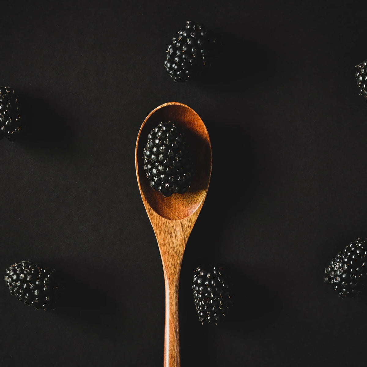 Fresh blackberries on black background with one in a wooden spoon